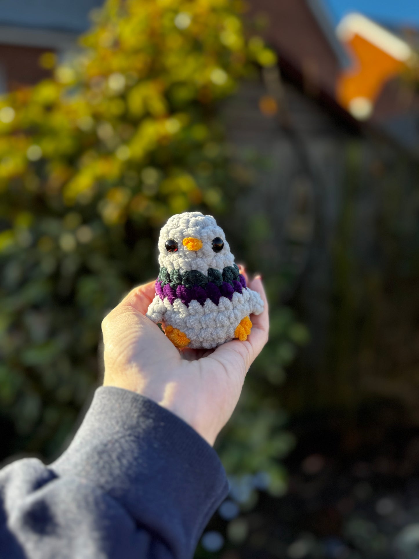 Hand holding a small crocheted owl toy outdoors with greenery in the background