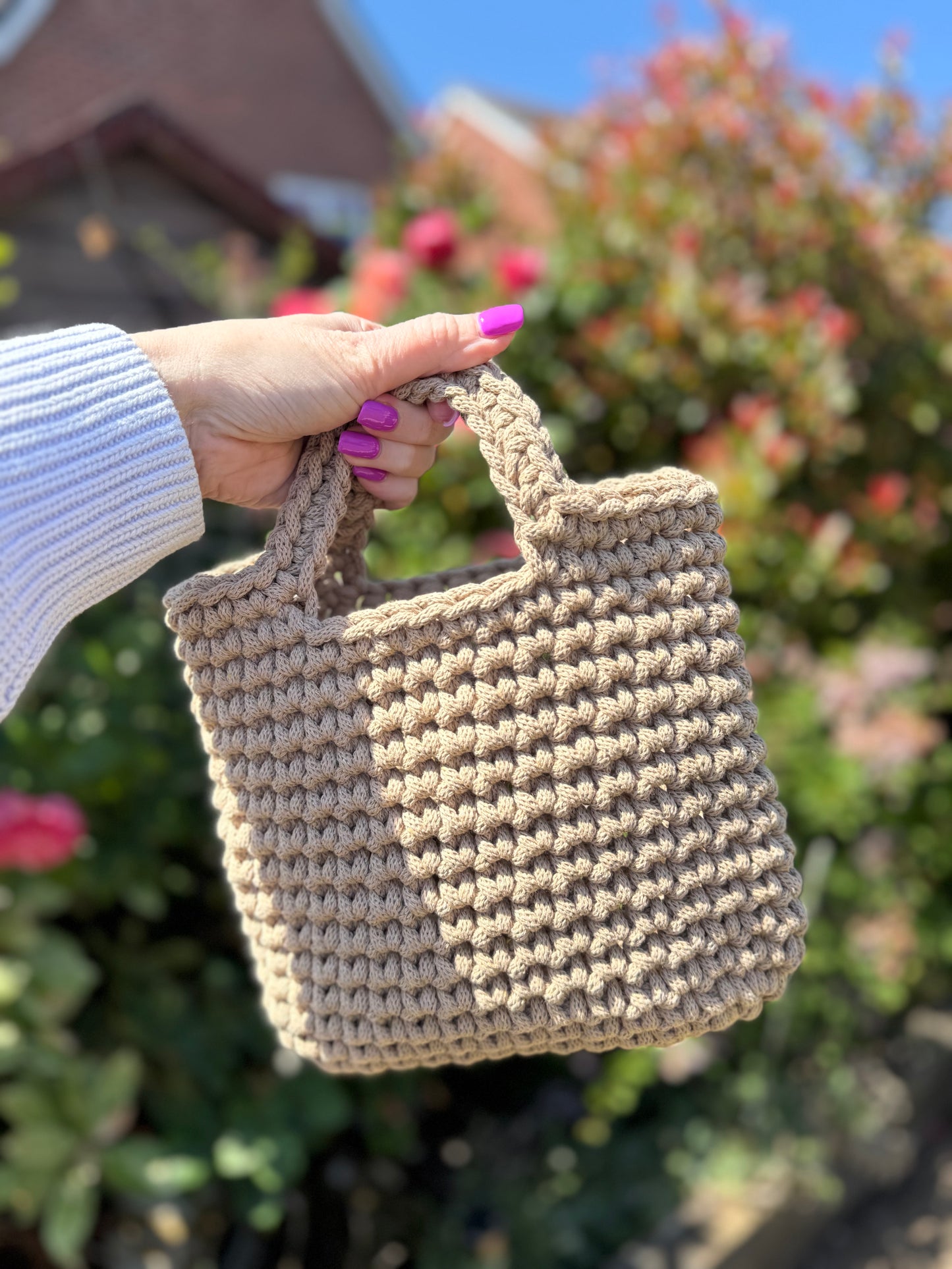 Hand holding a beige crochet bag with a blurred outdoor background
