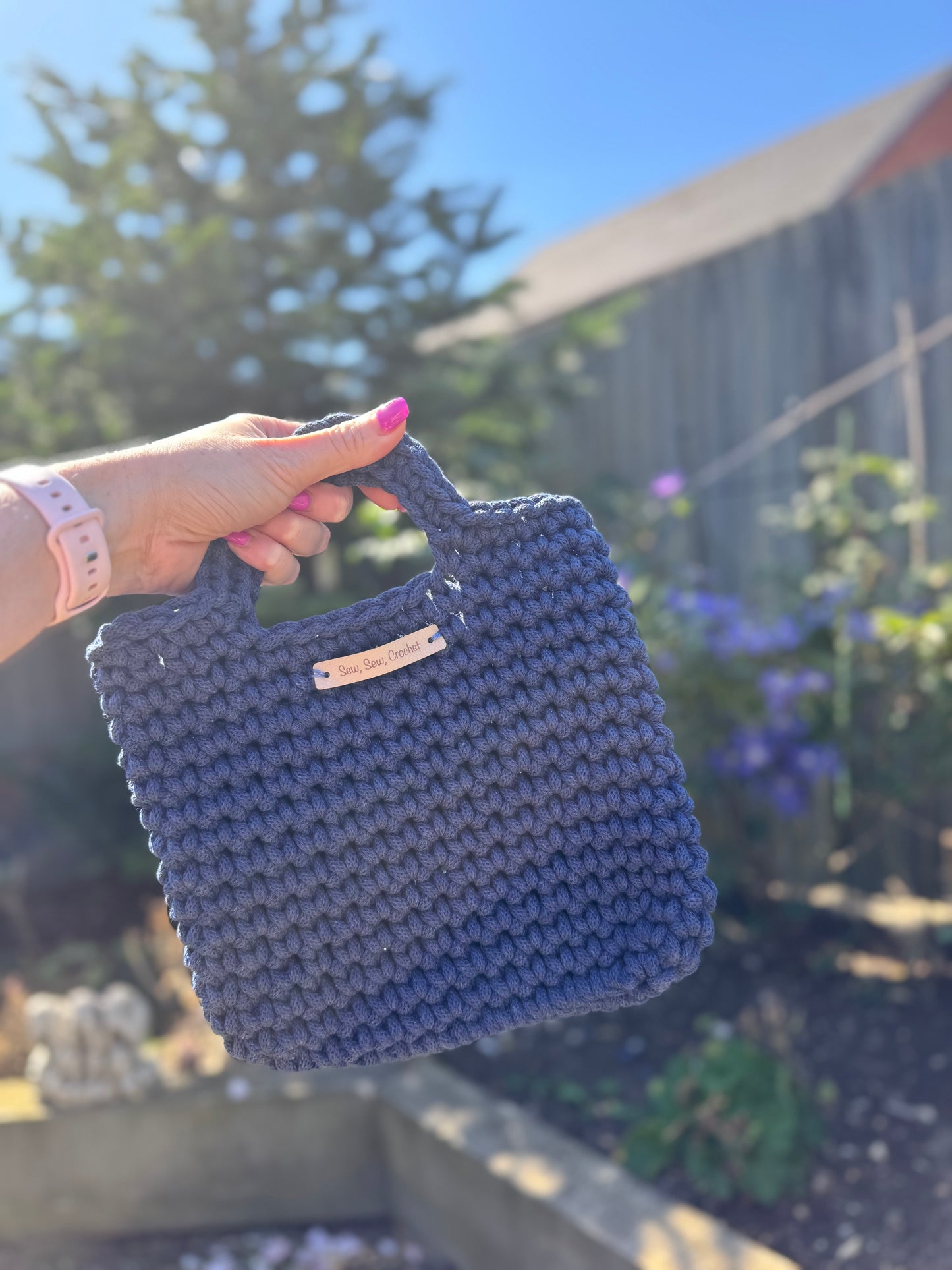Hand holding a blue crocheted bag with a blurred outdoor background