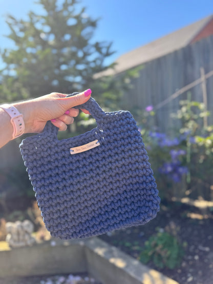 Hand holding a blue crocheted bag with a blurred outdoor background