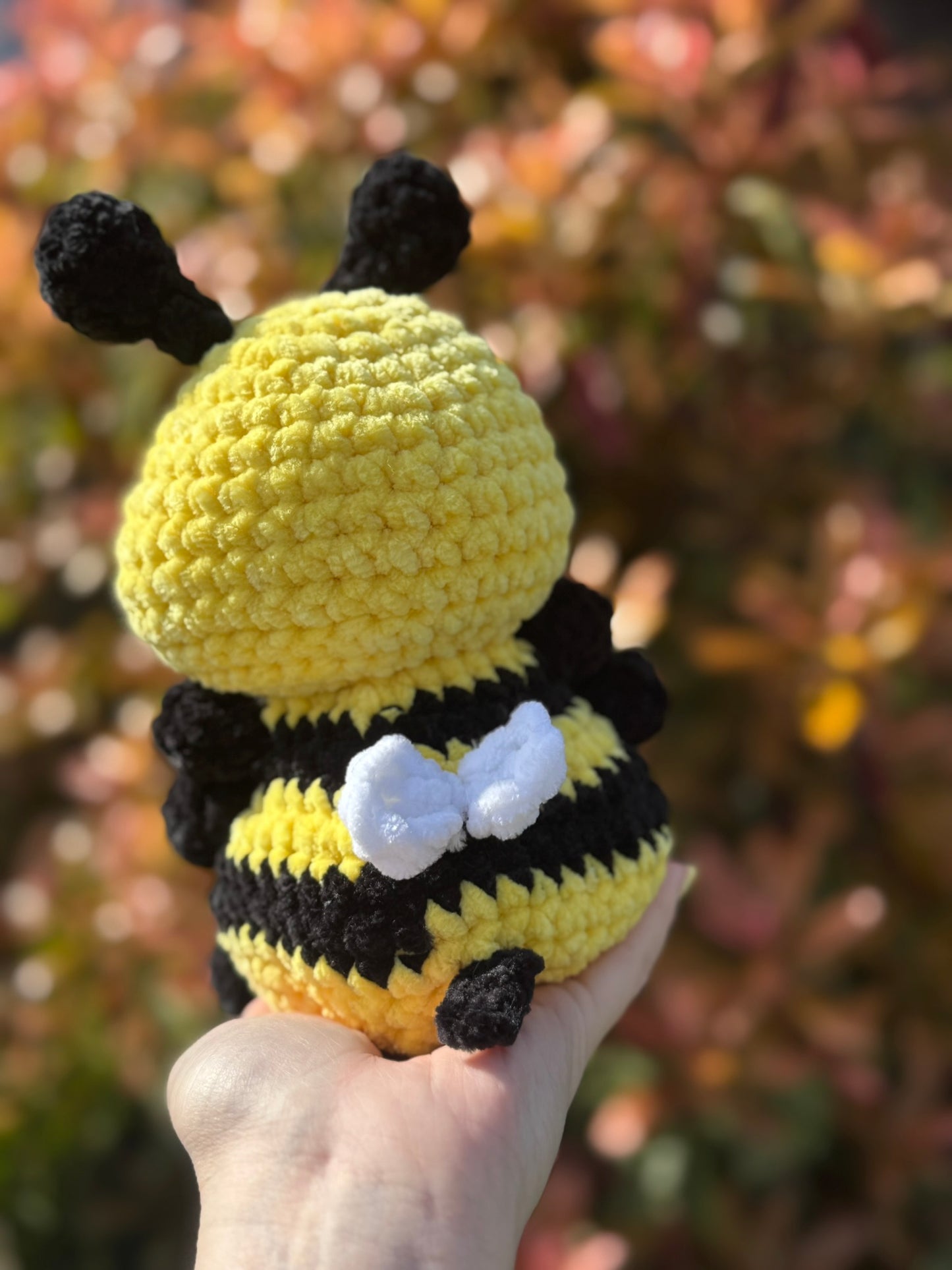 Hand holding a crochet bee toy with a blurred natural background