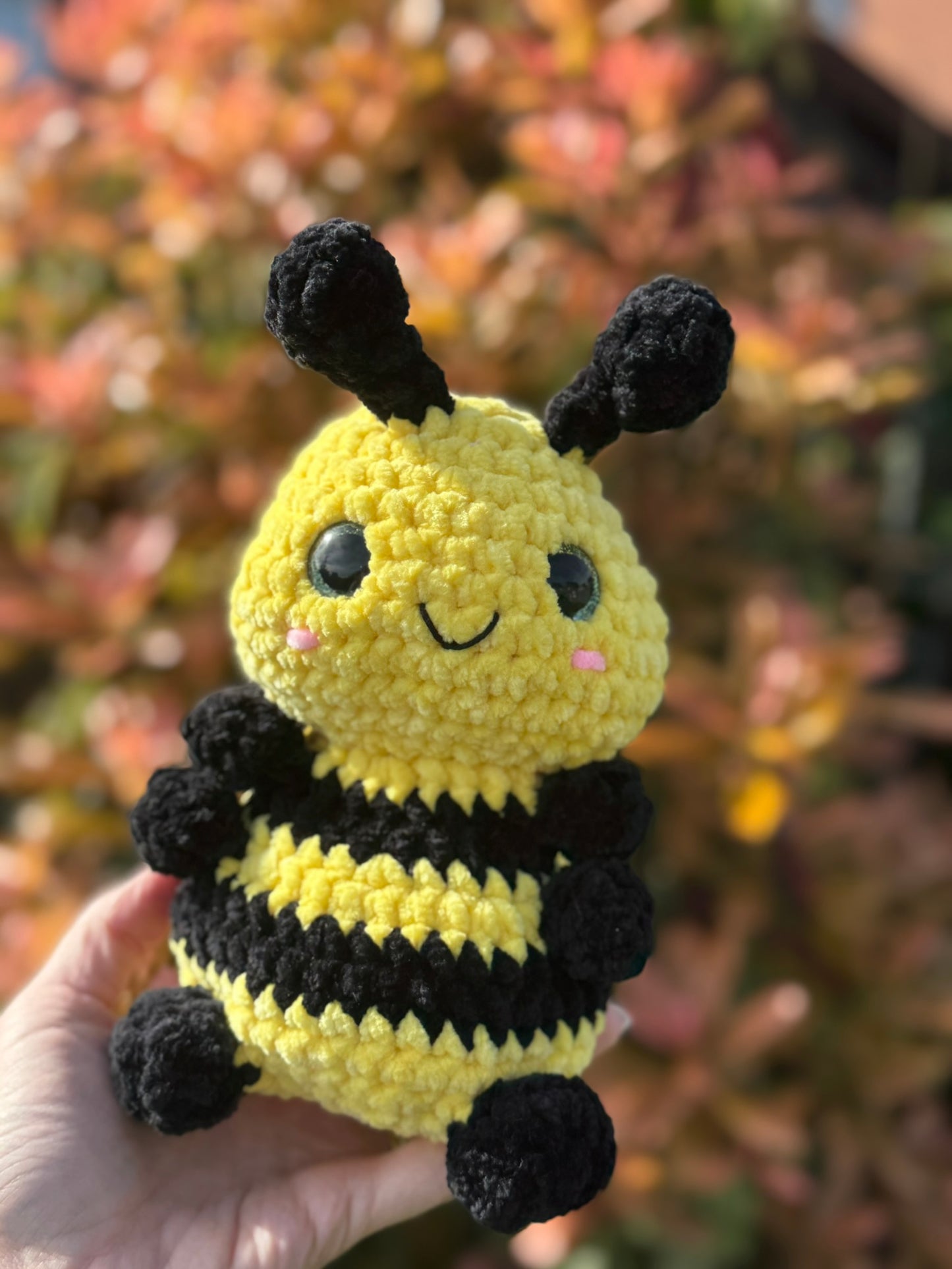 Crocheted bee toy held in a hand with a blurred natural background