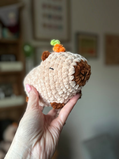 Hand holding a small crochet animal toy with a carrot on a blurred indoor background
