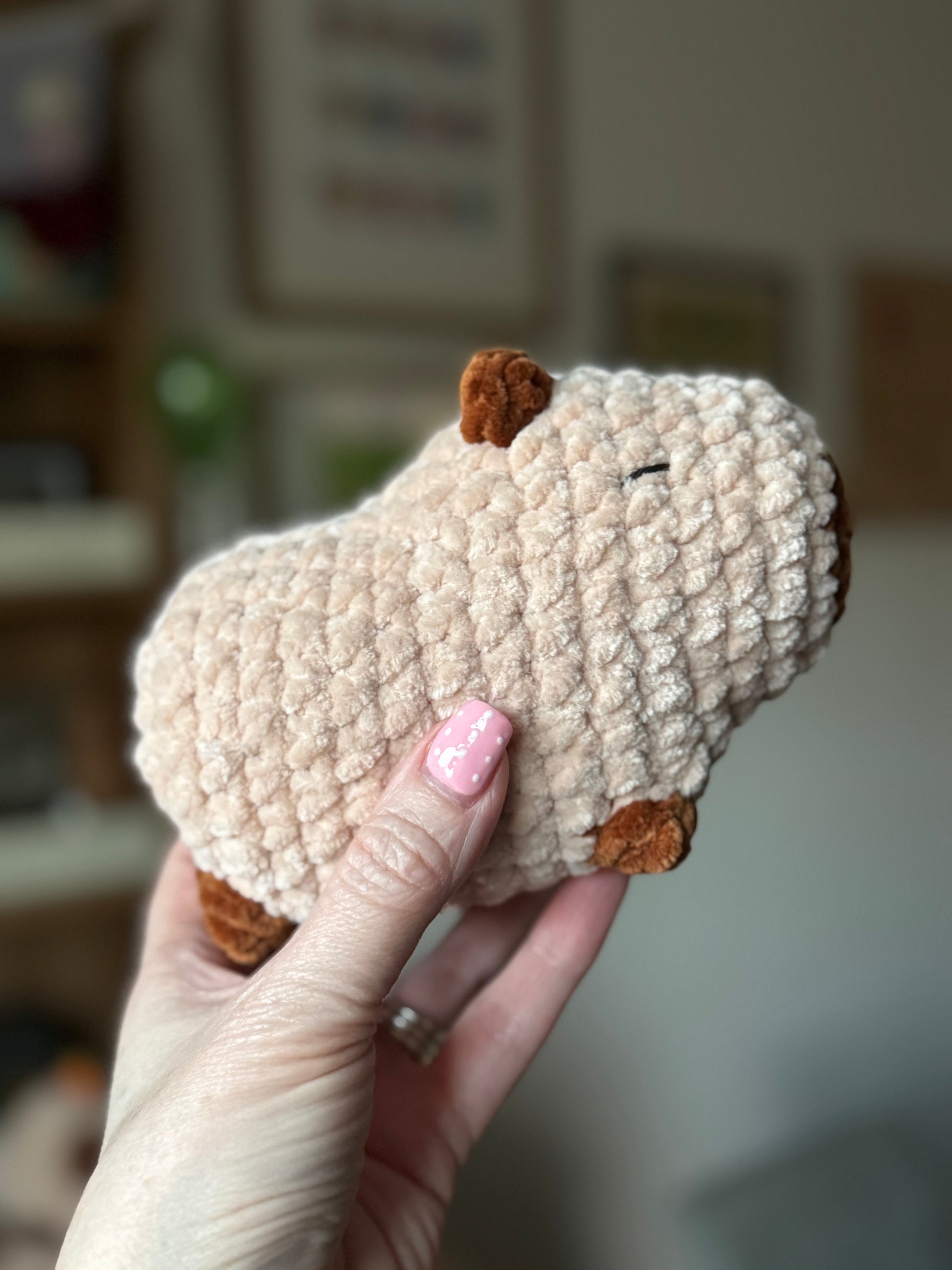 Hand holding a small, crocheted capybara animal toy with a blurred background