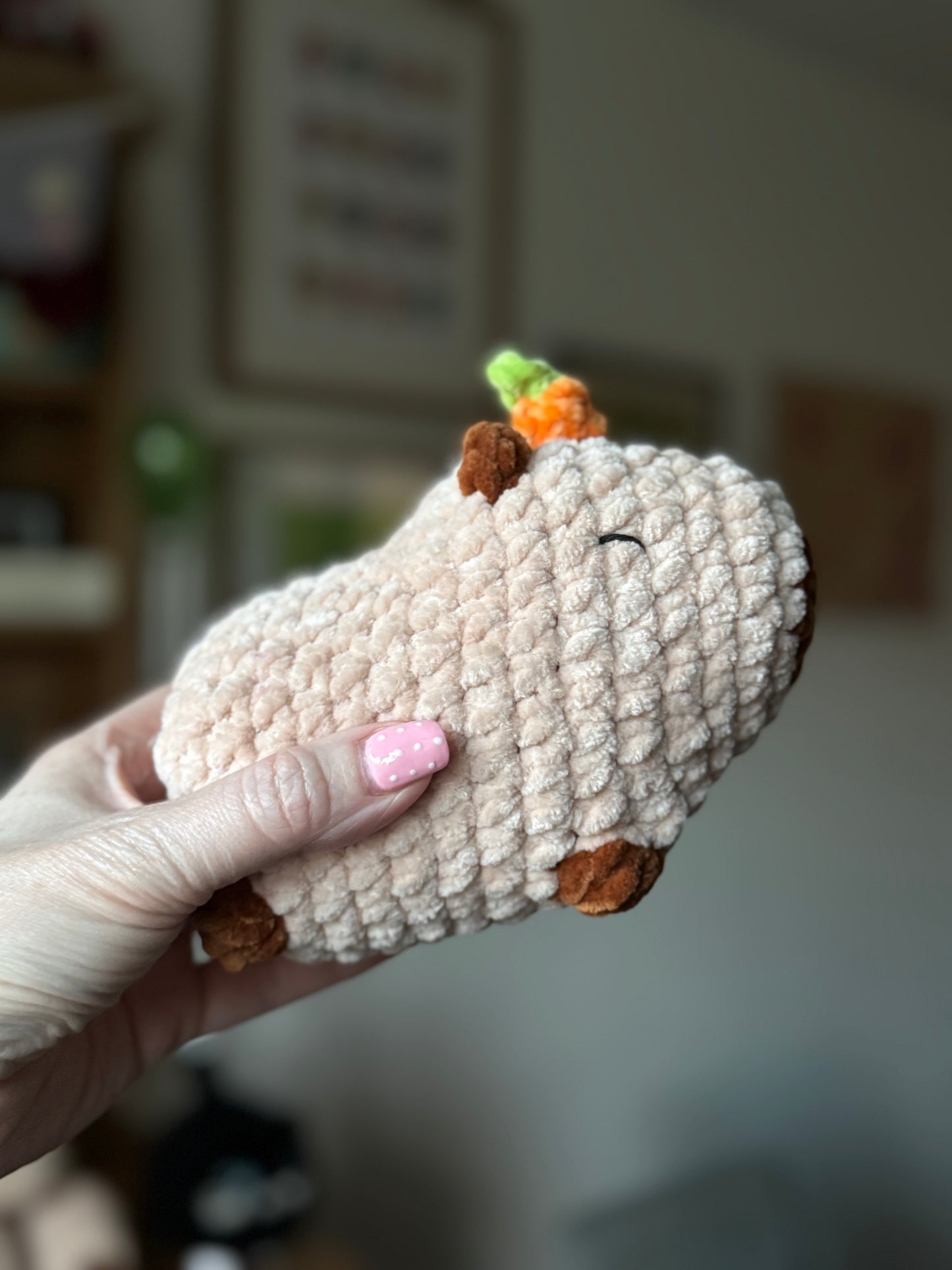 Hand holding a crocheted capybara sheep toy with an orange on its head indoor background