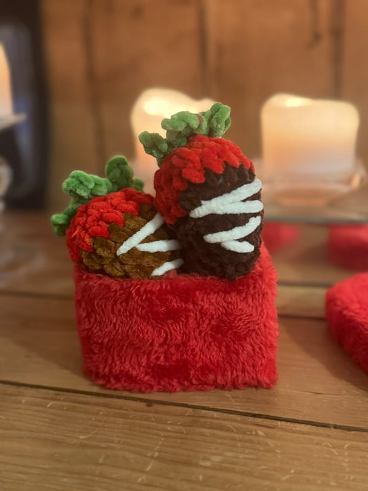 Red plush toy with chocolate-dipped strawberries on a wooden surface with blurred candles in the background