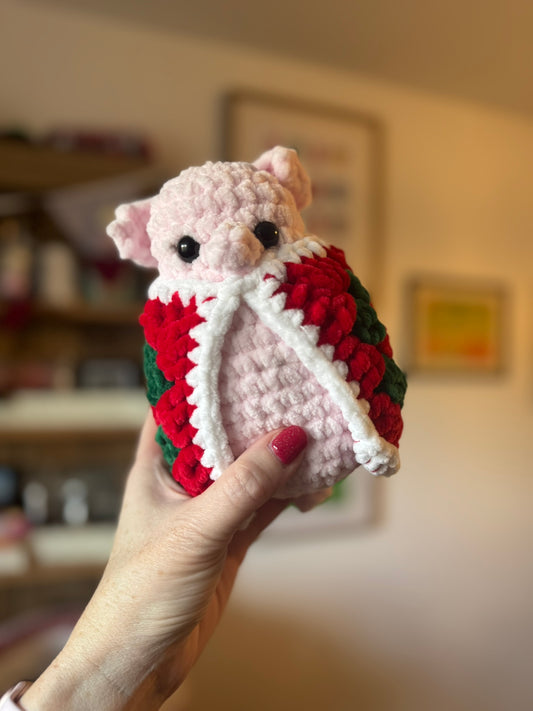 a cute crochet pig in a red and green blanket.  Hand held size.  