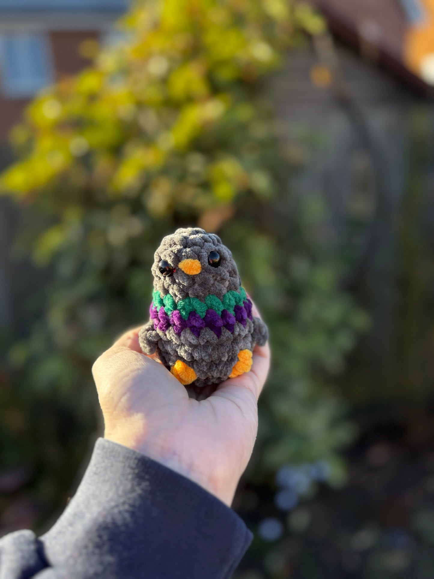 Hand holding a small crocheted owl toy with a blurred outdoor background