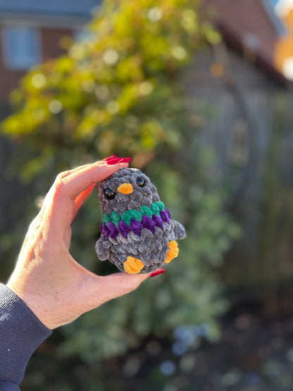 Hand holding a small crocheted penguin toy with a blurred outdoor background