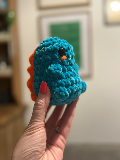 Blue crocheted toy held by a hand with red nail polish, blurred indoor background