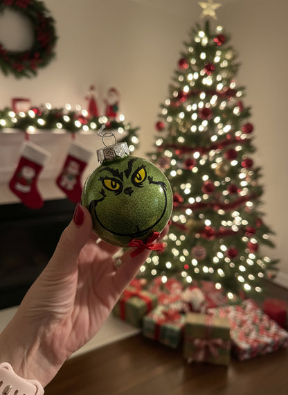 Hand holding a green ornament with a face, blurred indoor background