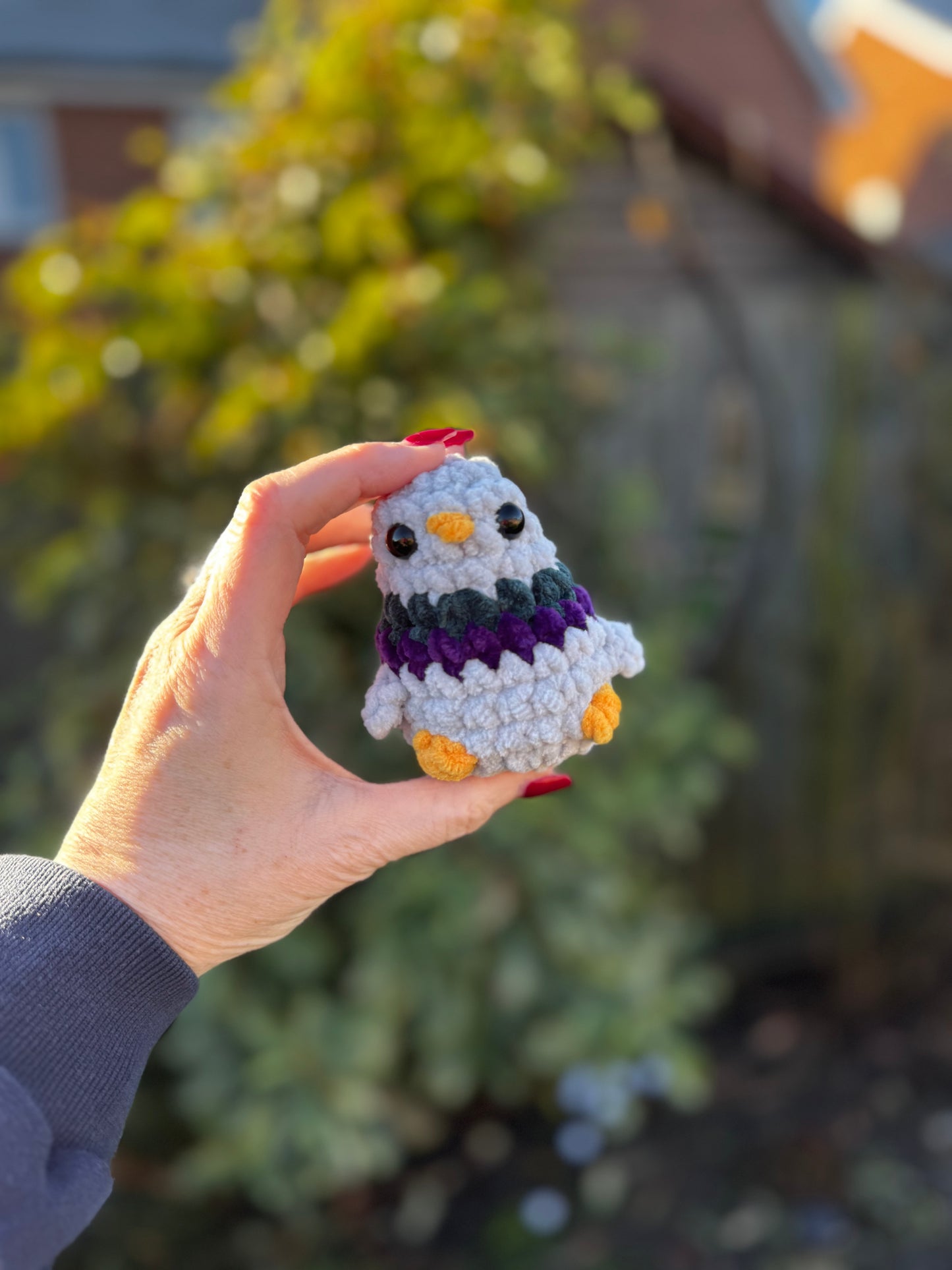 Hand holding a small crochet owl toy with a blurred outdoor background
