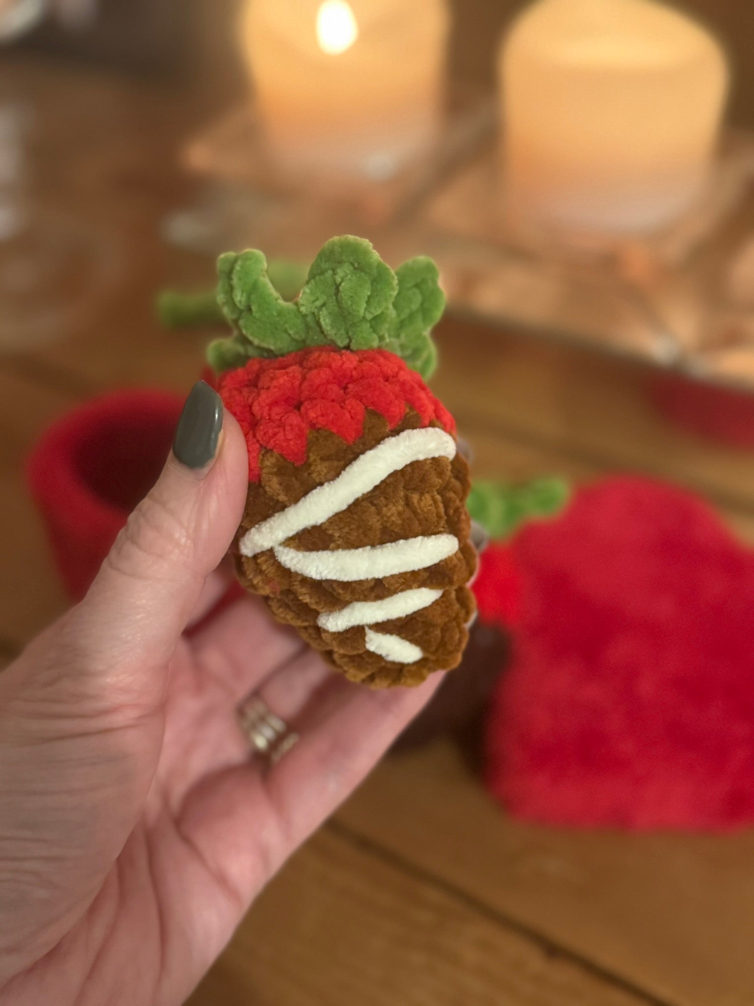 Hand holding a felt strawberry toy with a blurred background