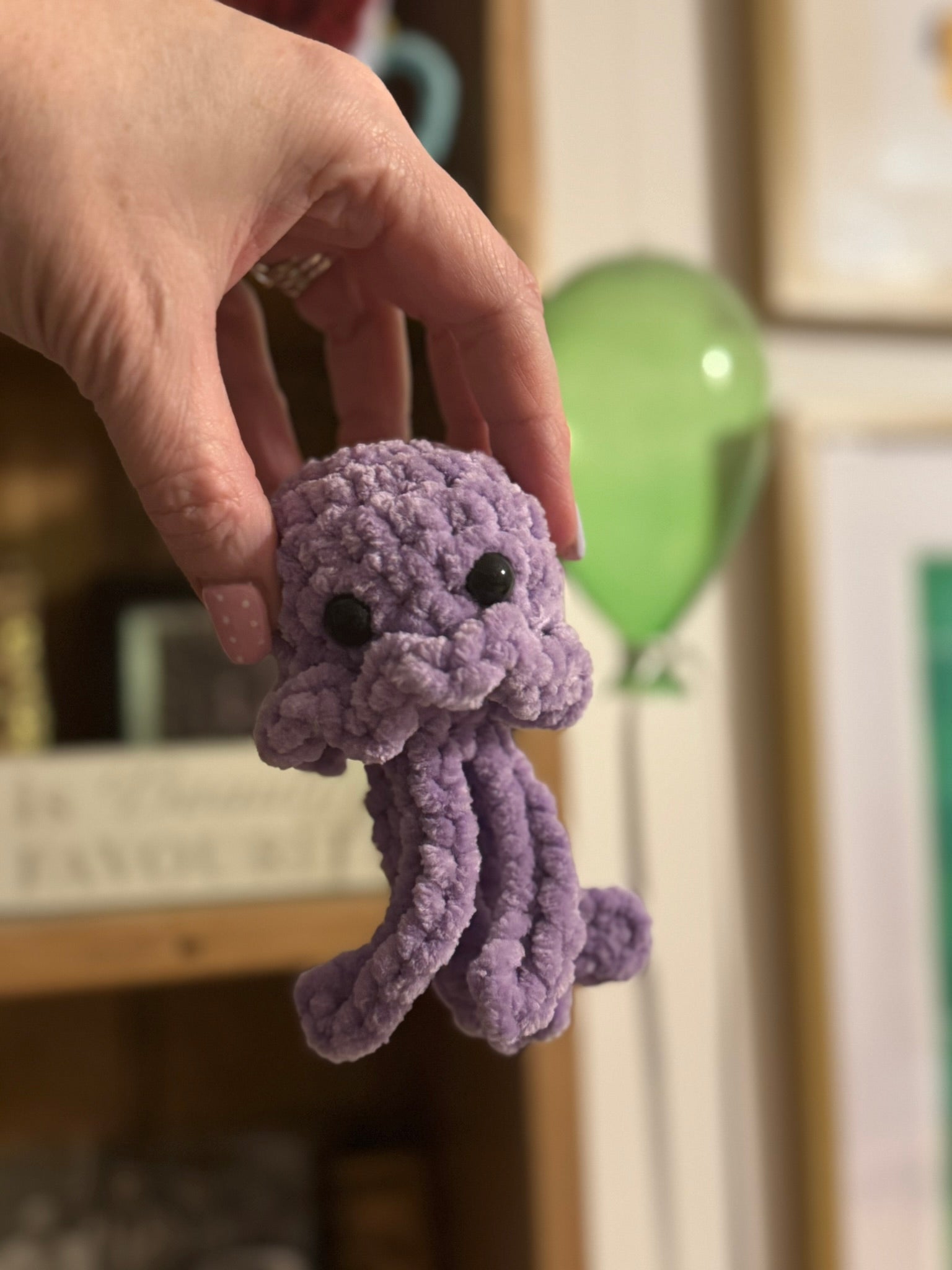 Purple crocheted octopus toy held by a hand in a blurred indoor setting