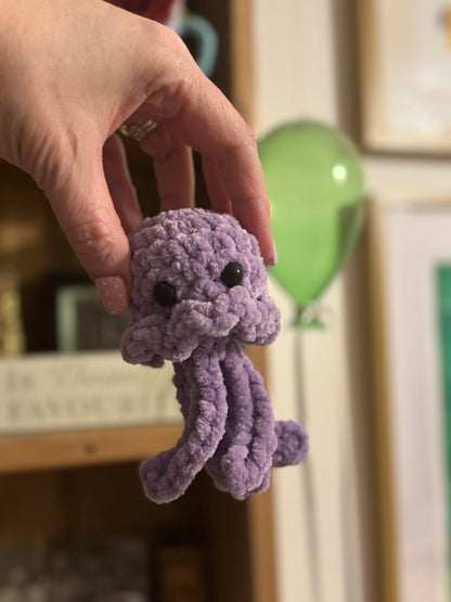 Purple crocheted octopus toy held by a hand in a blurred indoor setting
