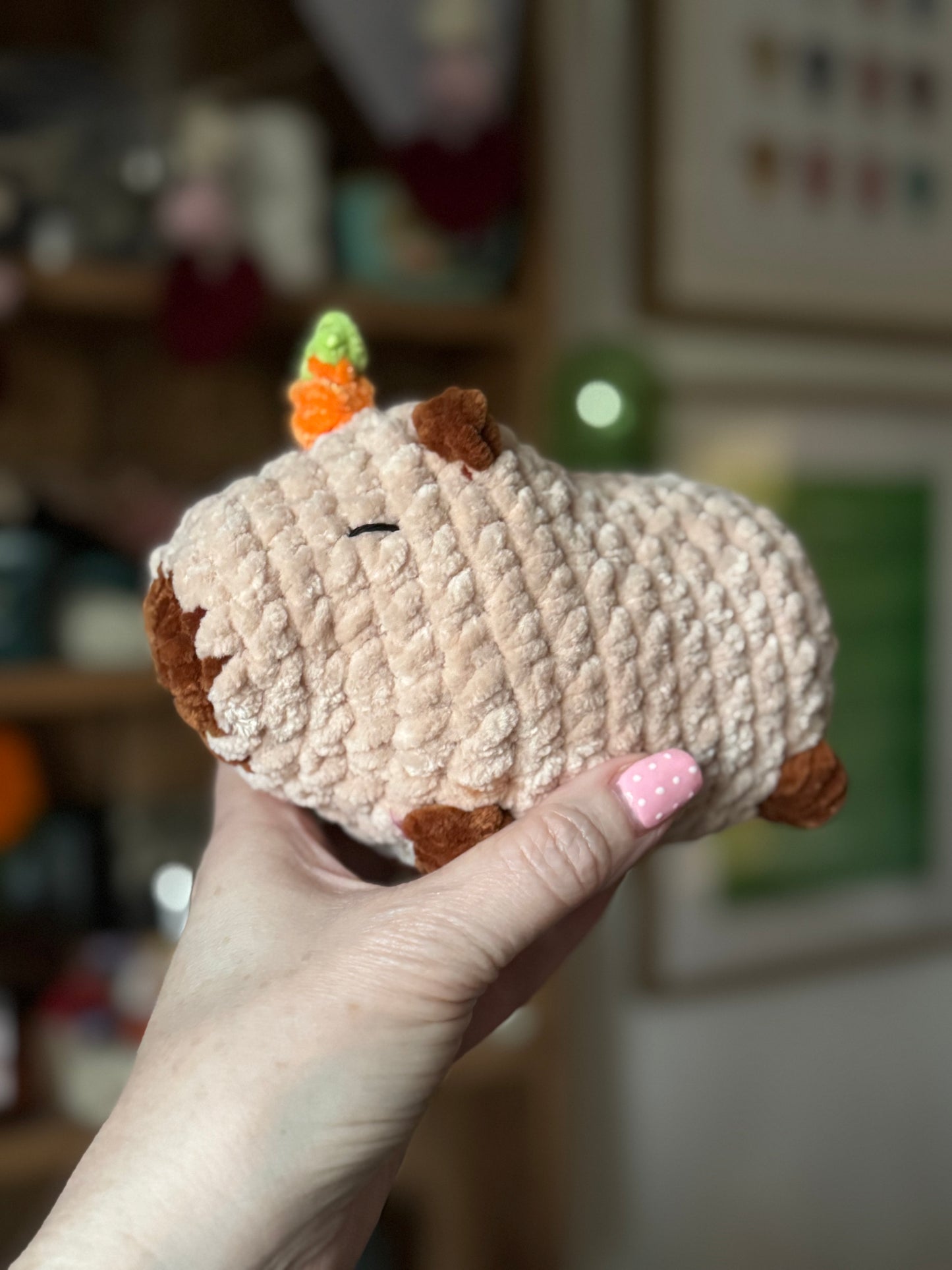 Hand holding a small plush capybara resembling a sheep with an orange on a blurred background