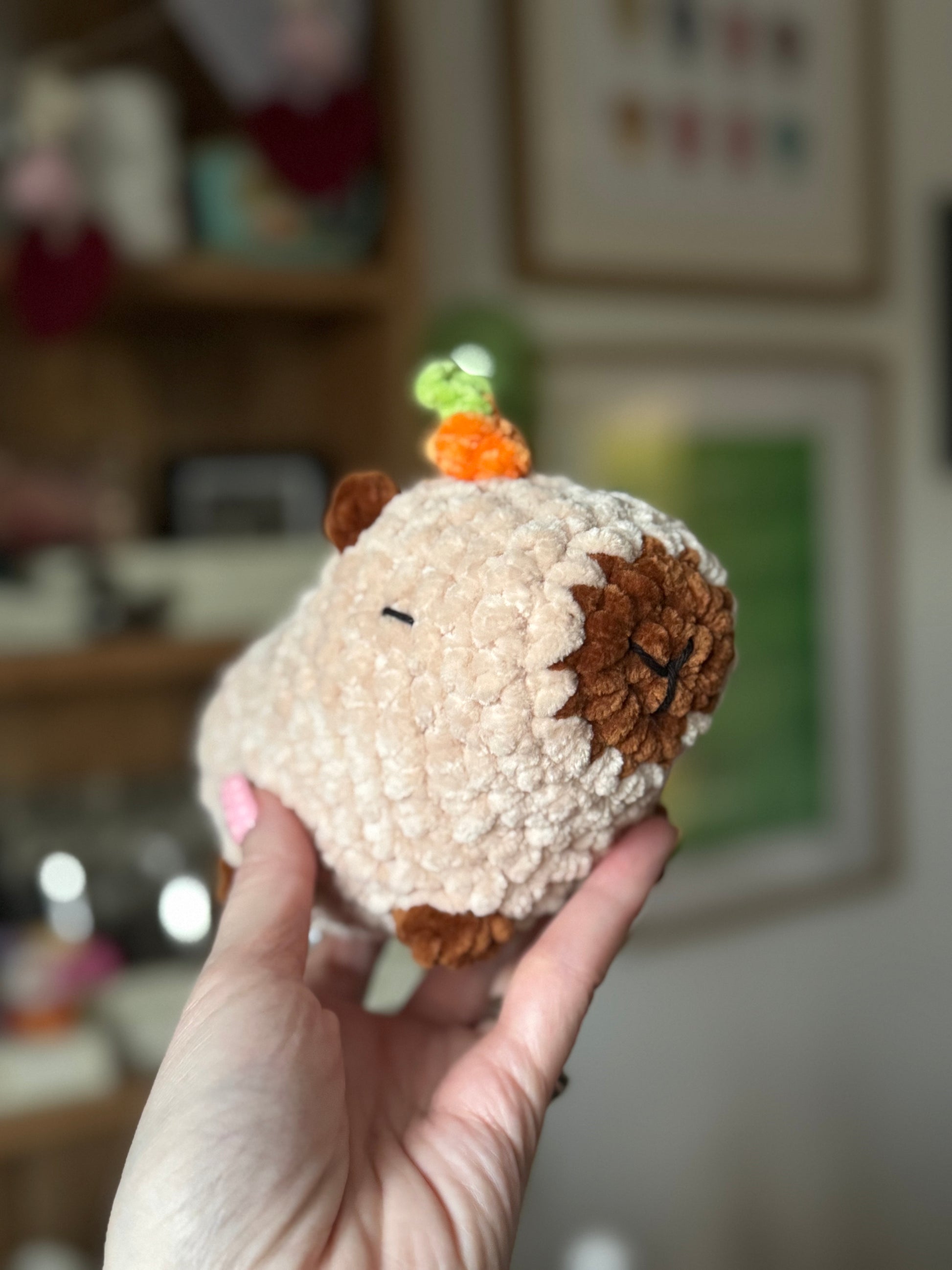 Hand holding a small plush capybara resembling with a blurred indoor background