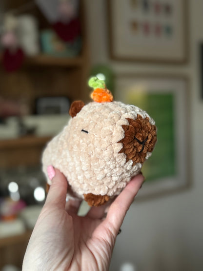 Hand holding a small plush capybara resembling with a blurred indoor background