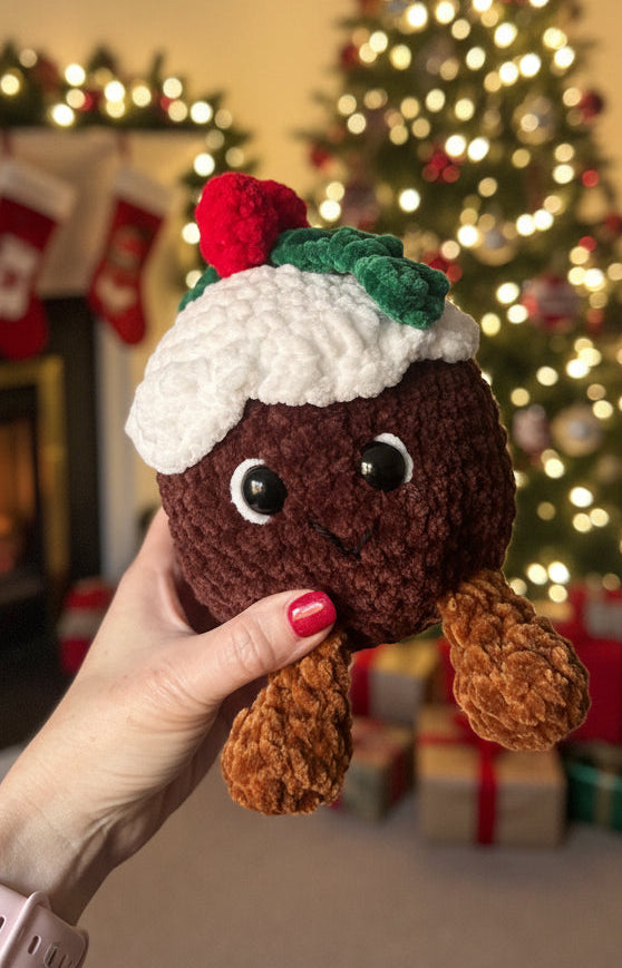 Hand holding a small crocheted Christmas pudding toy with a blurred indoor background