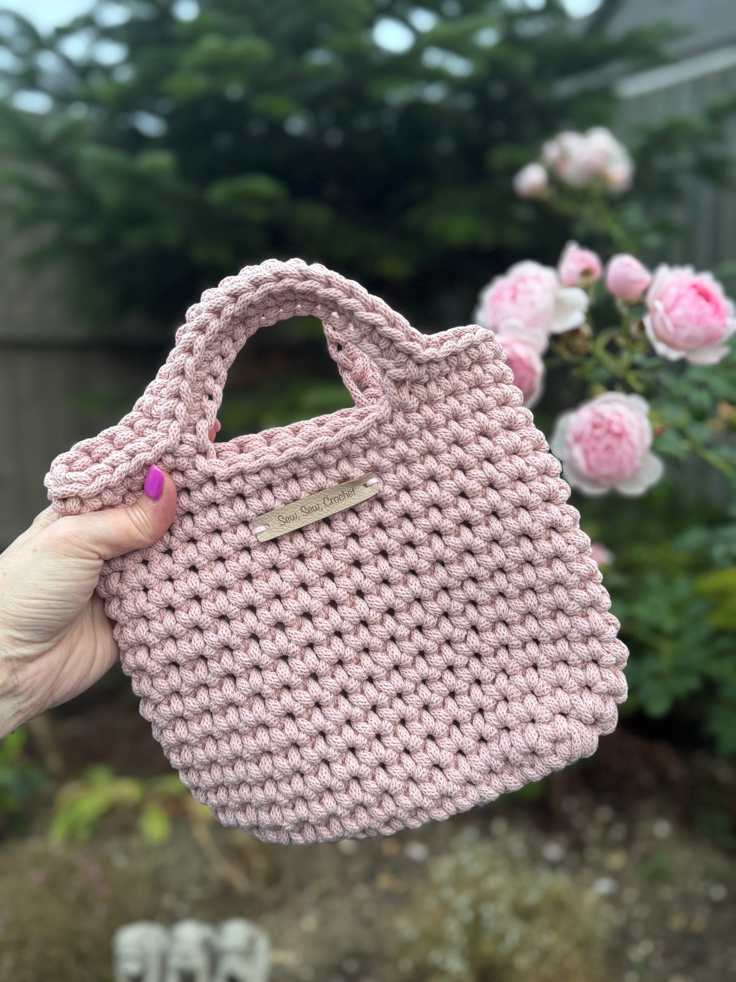 Pink crocheted bag held by a hand with a blurred garden background