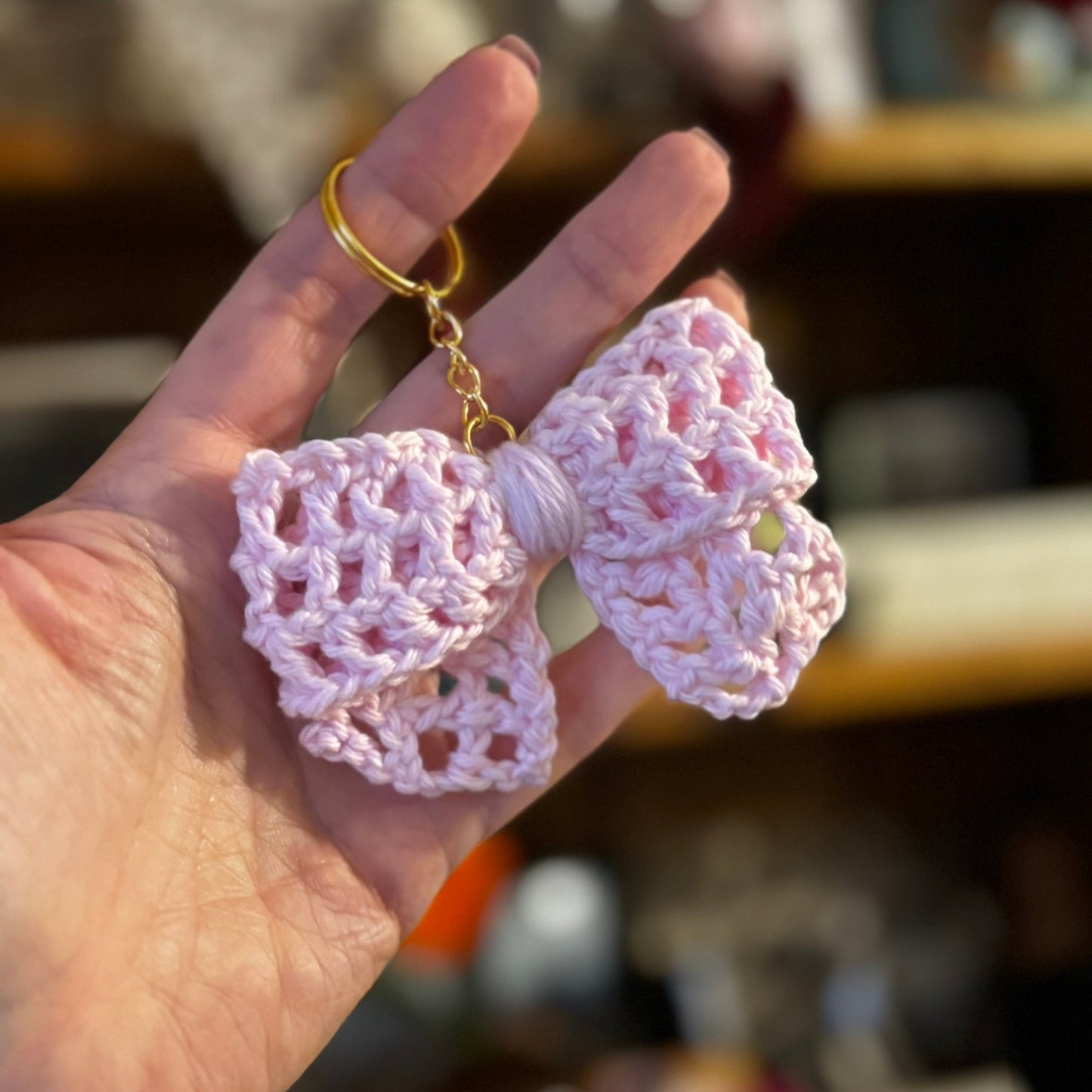 Hand holding a pink crocheted bow keychain against a blurred background