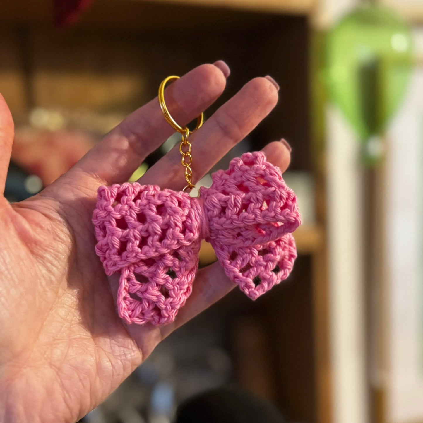 Hand holding a pink crocheted keychain with a blurred background