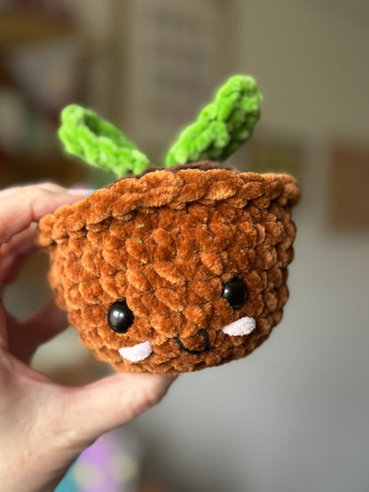 Small crocheted plant toy with a face held in a hand against a blurred background