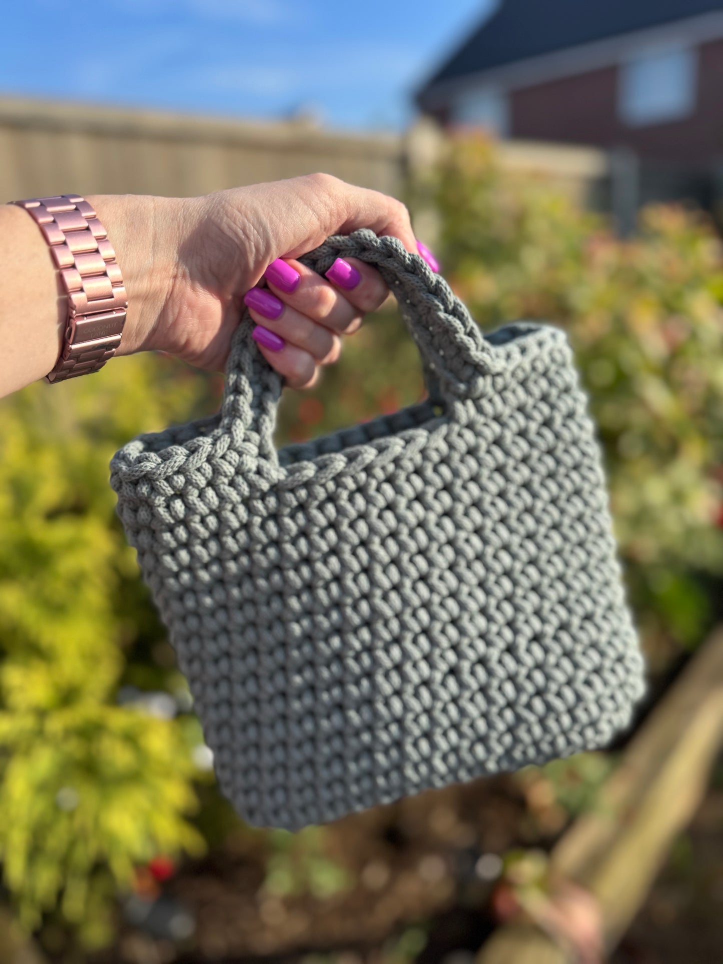 Person holding a sage knitted handbag with a blurred outdoor background