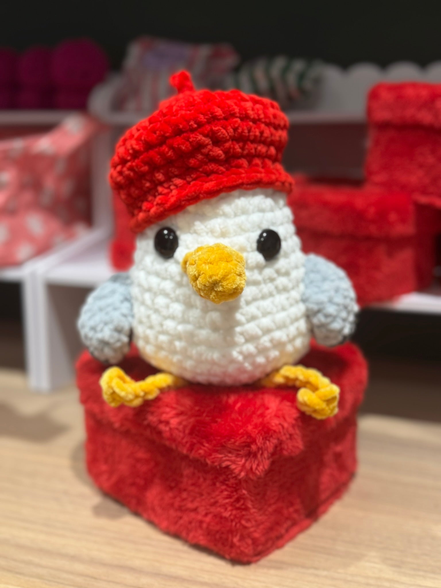 Crocheted penguin toy with a red hat and scarf on a wooden surface.