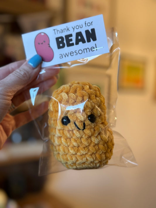 Small plush toy with a face in a clear package held by a hand, with a 'Thank you for BEAN awesome!' tag.