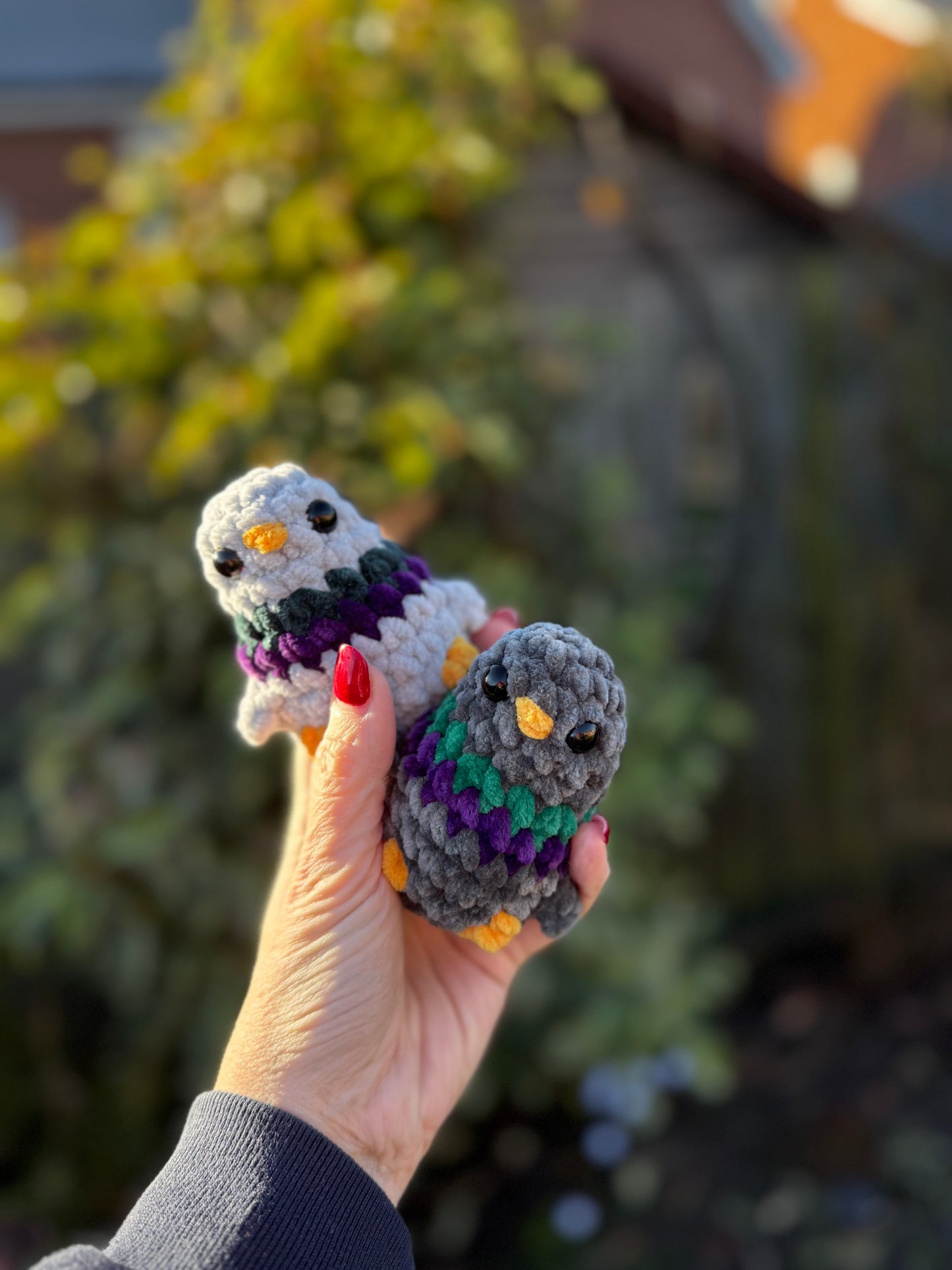 Hand holding two small crochet animals against a blurred natural background