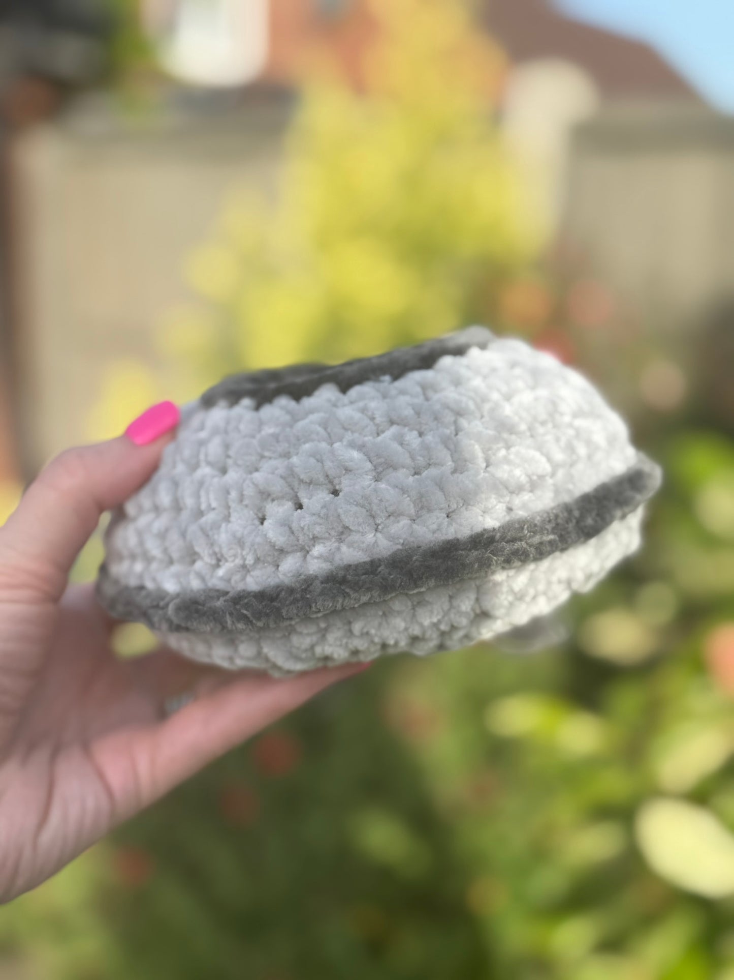 Hand holding a textured gray and white ufo against a blurred outdoor background